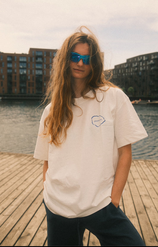 Model wearing white GRANITE. ESSENTIAL tee with blue GRANITE. logo on the chest and in the back